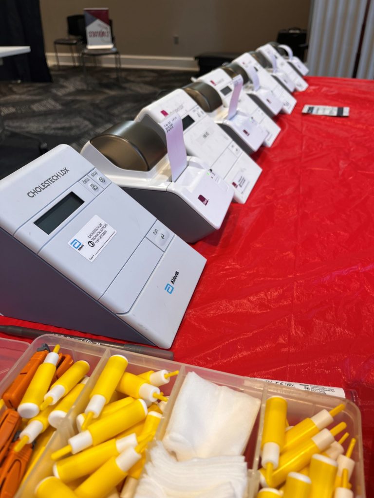 table with a red table cloth and lipid profile machines in a row with printers attached that have printed blood work results on a sticker.