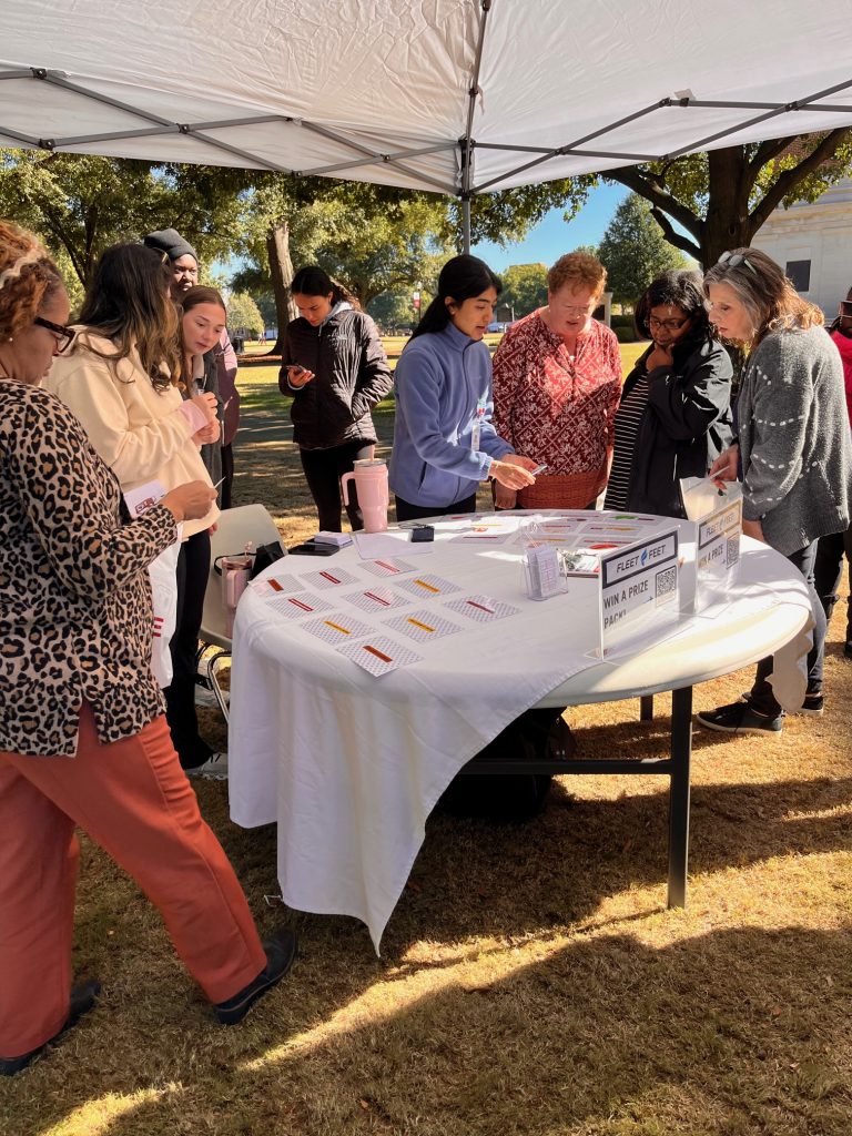 UA employees standing around a table with white table cloth playing a matching game with cards and discussing results with students