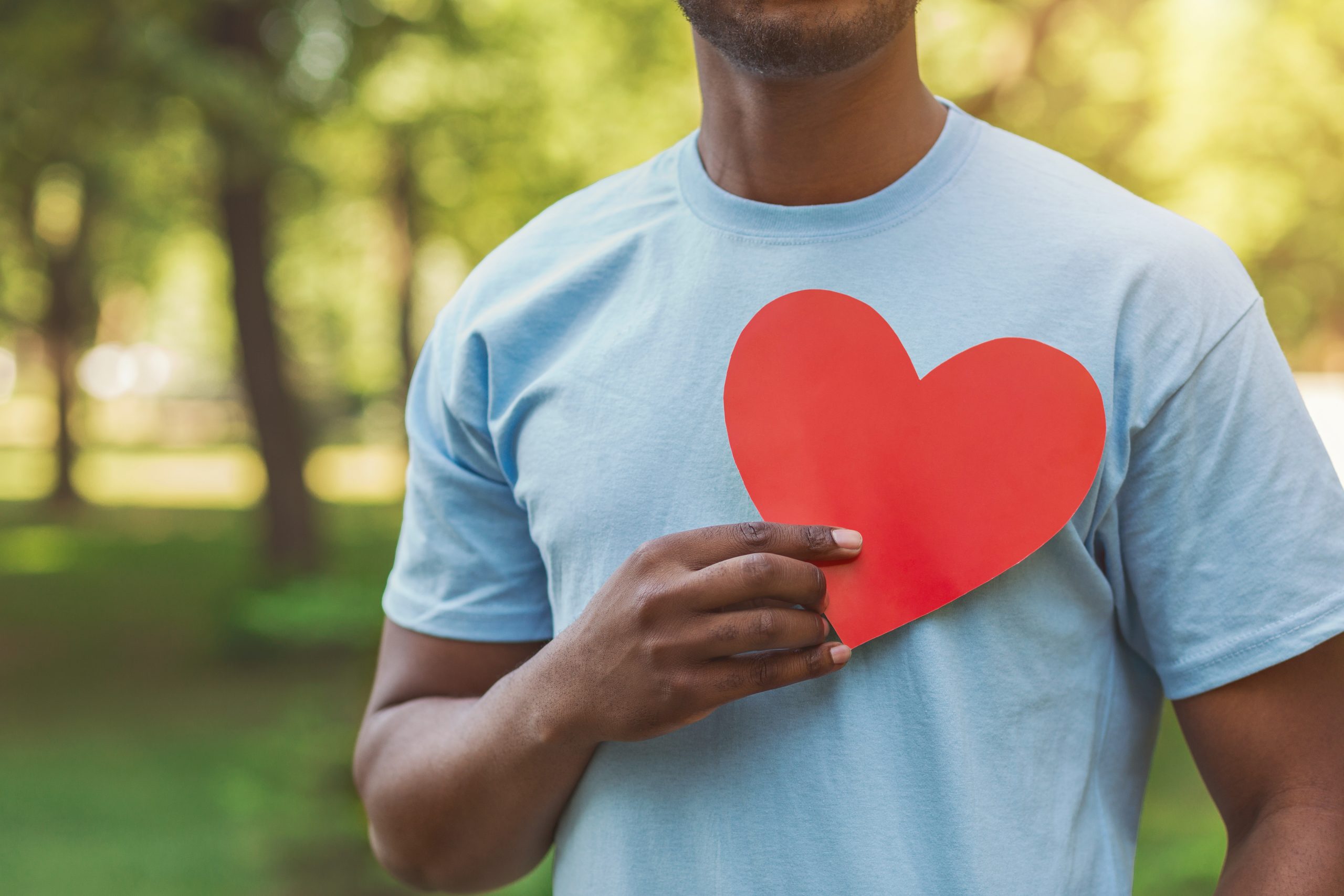 World heart day, volunteering and charity. Millennial african-american man holding red heart on his chest, free space