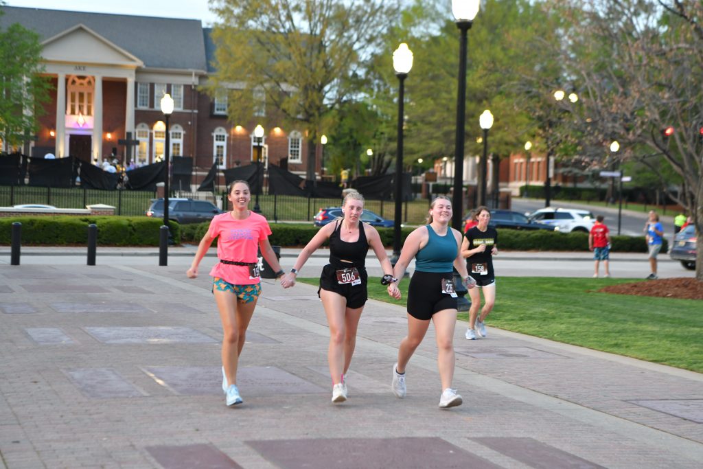 3 women holding hands running toward the finish line