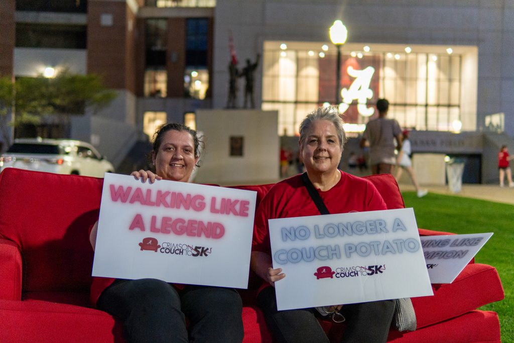 2 women sitting on red couch holding signs with running/walking phrases