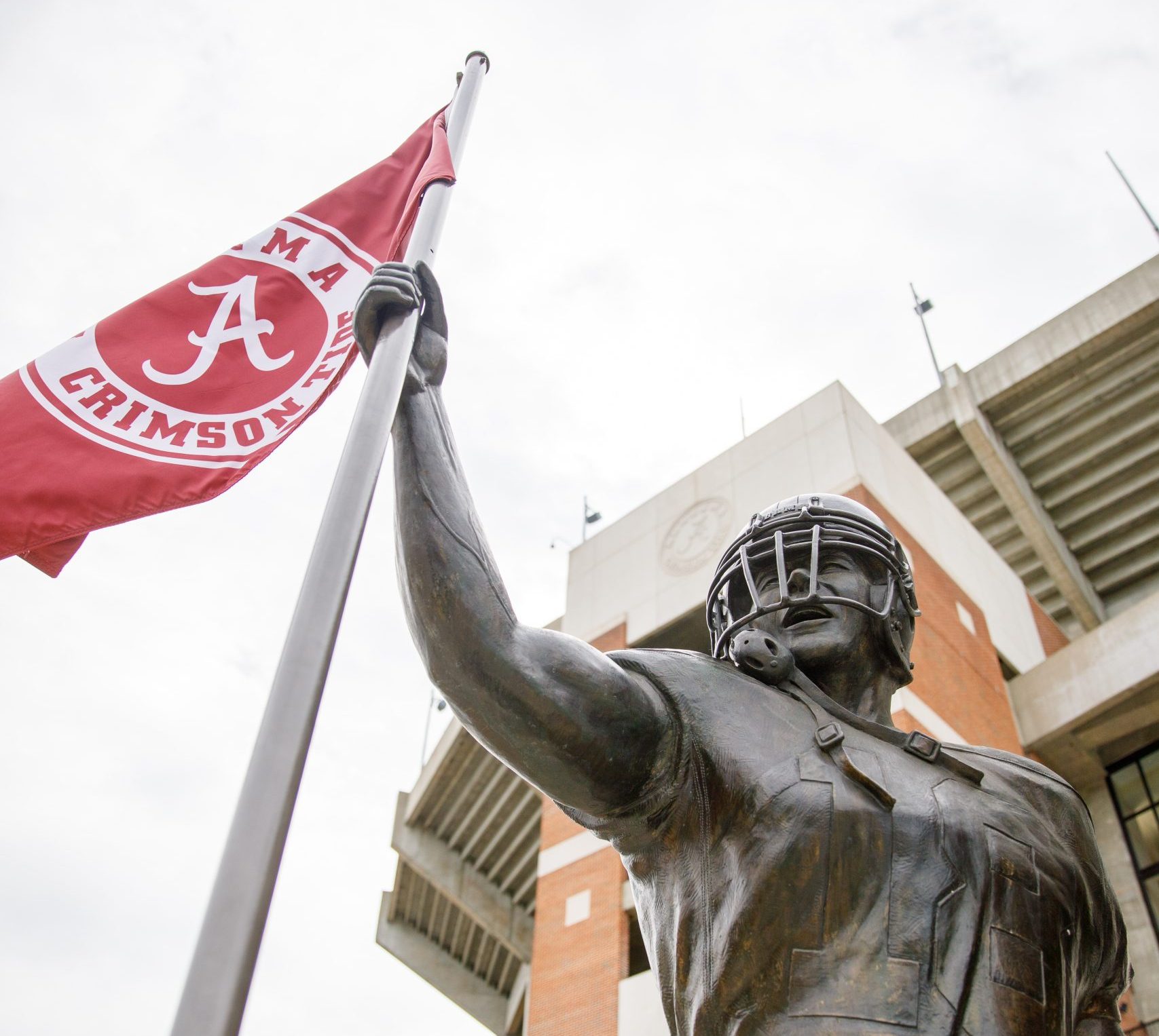 Statue of a football player holding a UA flag in front of Bryant Denny Stadium