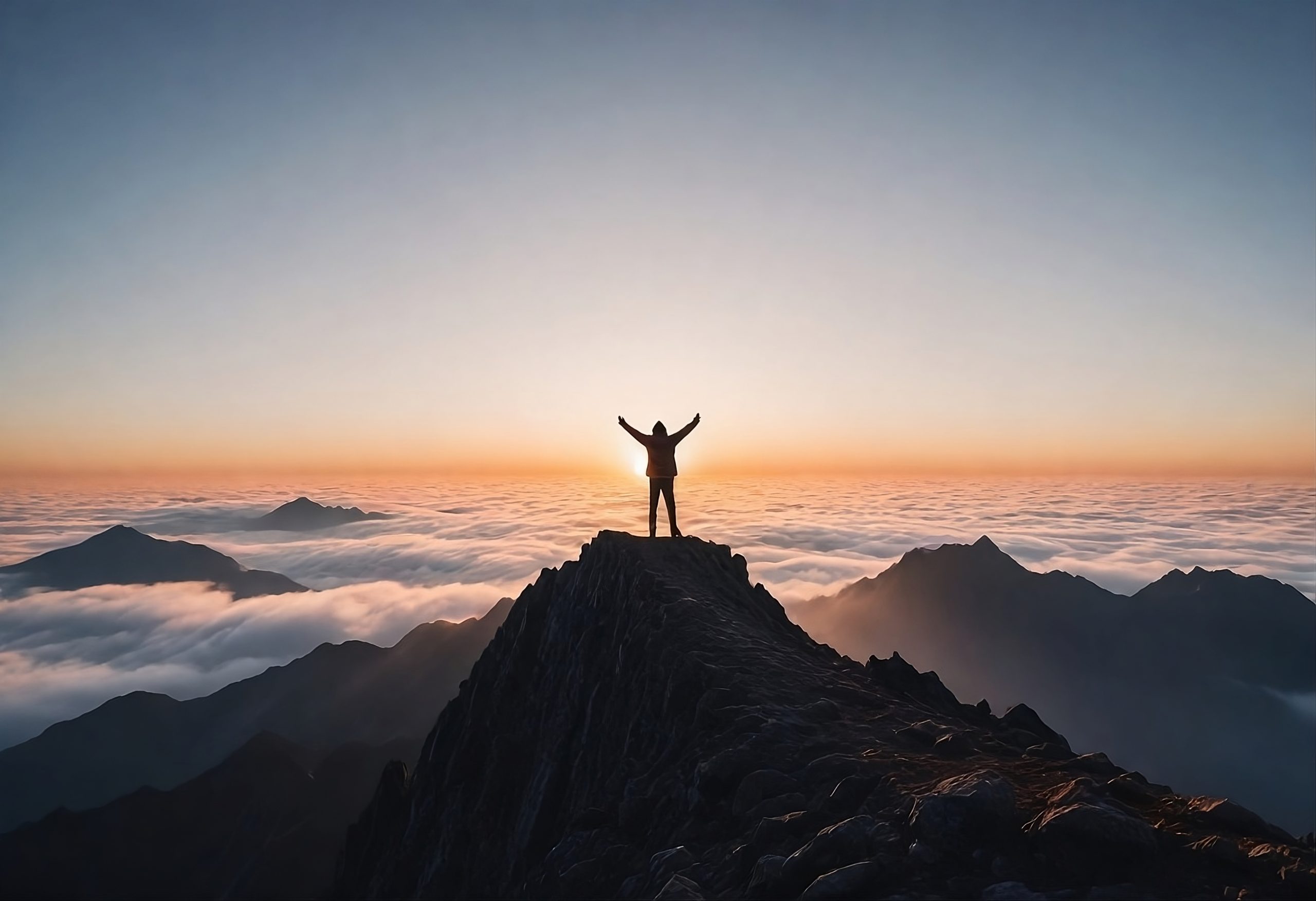 person standing on top of a mountain peak with arms raised, above the clouds during sunrise