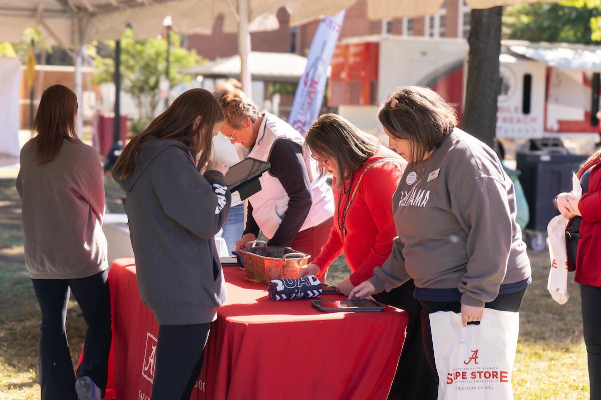 Women outside signing in at a table with a red table cloth holding Supestore plastic bags