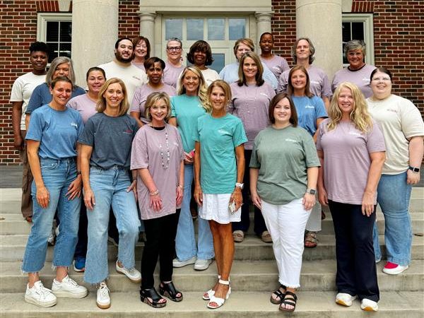 Large group of men and women standing outside a building with different colored t-shirts