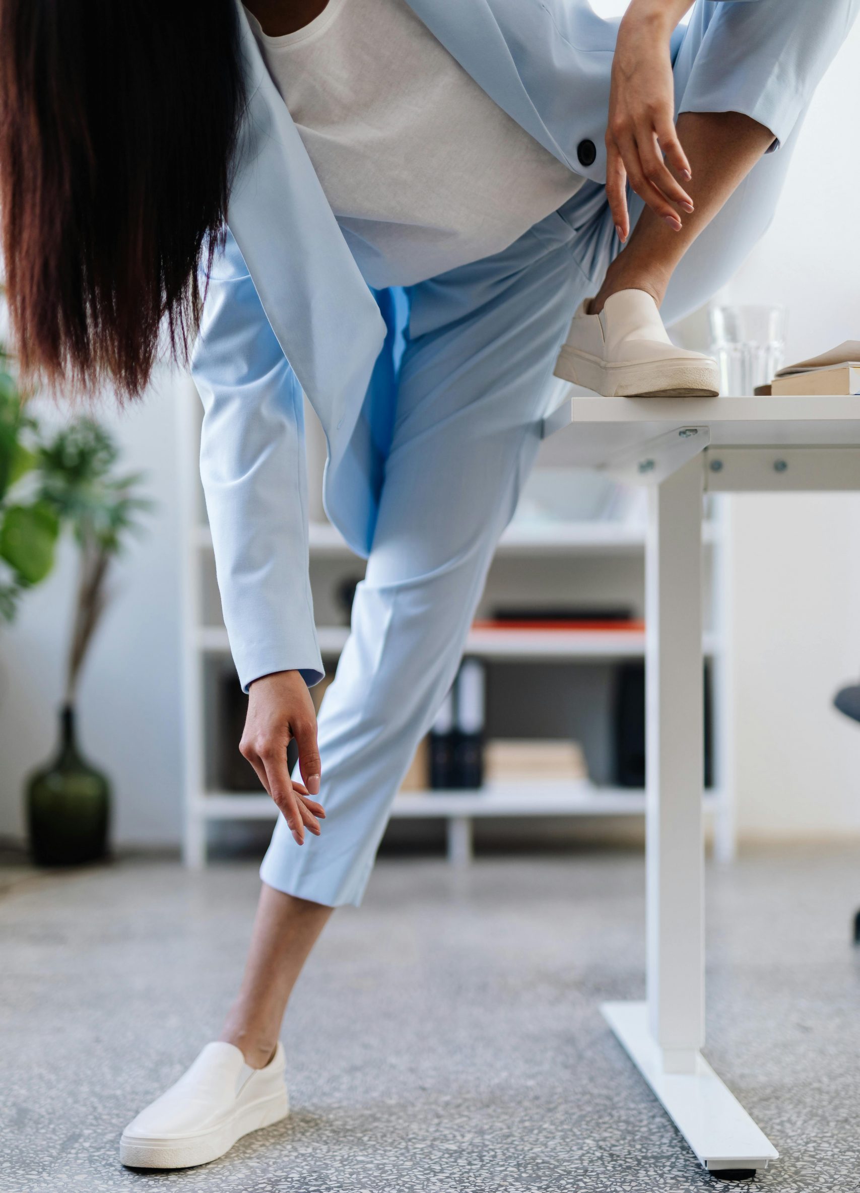 women in a light blue suit stretching at a desk with her foot on the desk top.