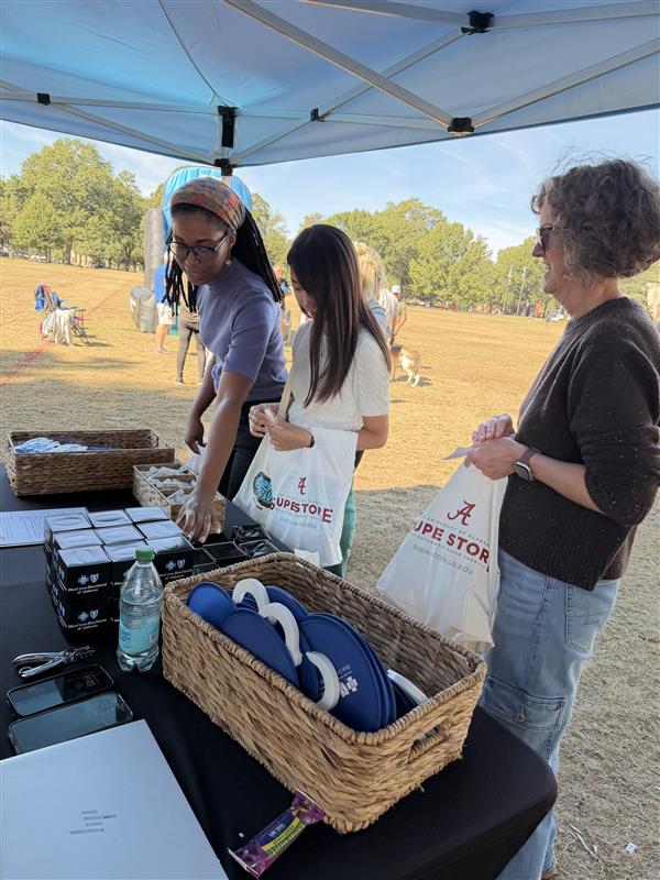 3 women stand at a table picking up mini tissue boxes and blue flexible outdoor fans