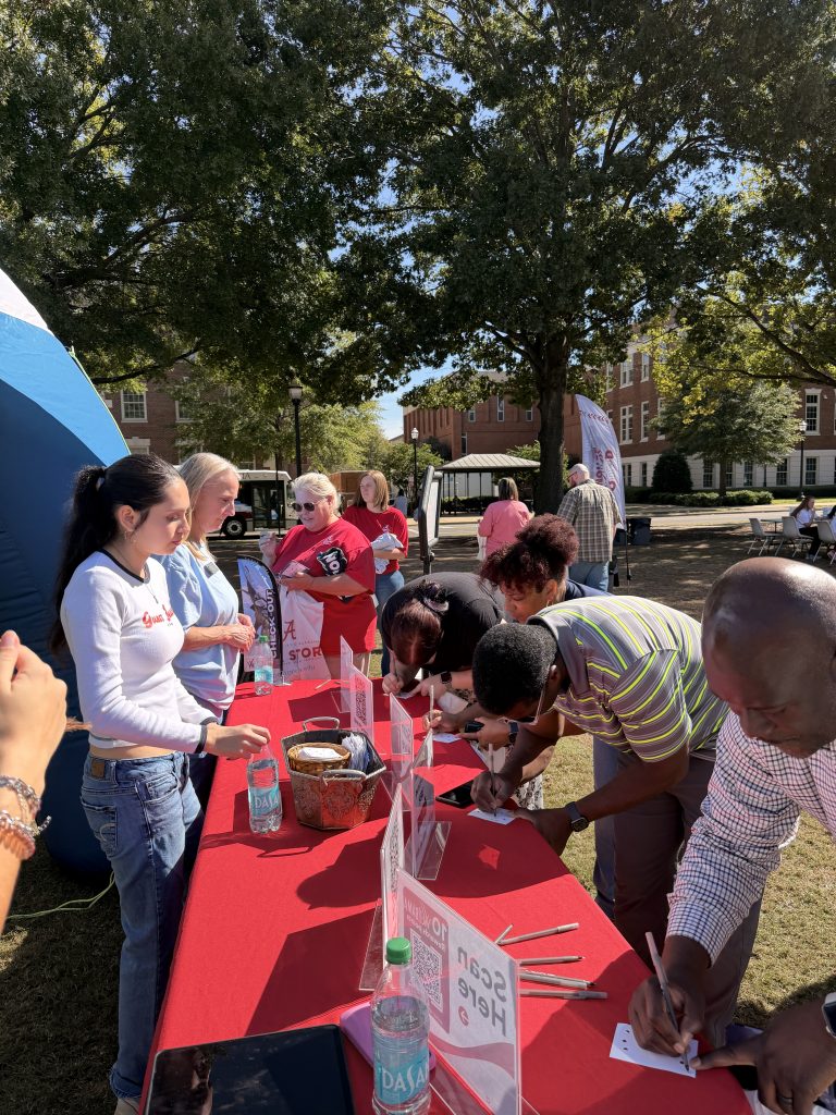 a group of people bend over a table to write on a piece of paper outside