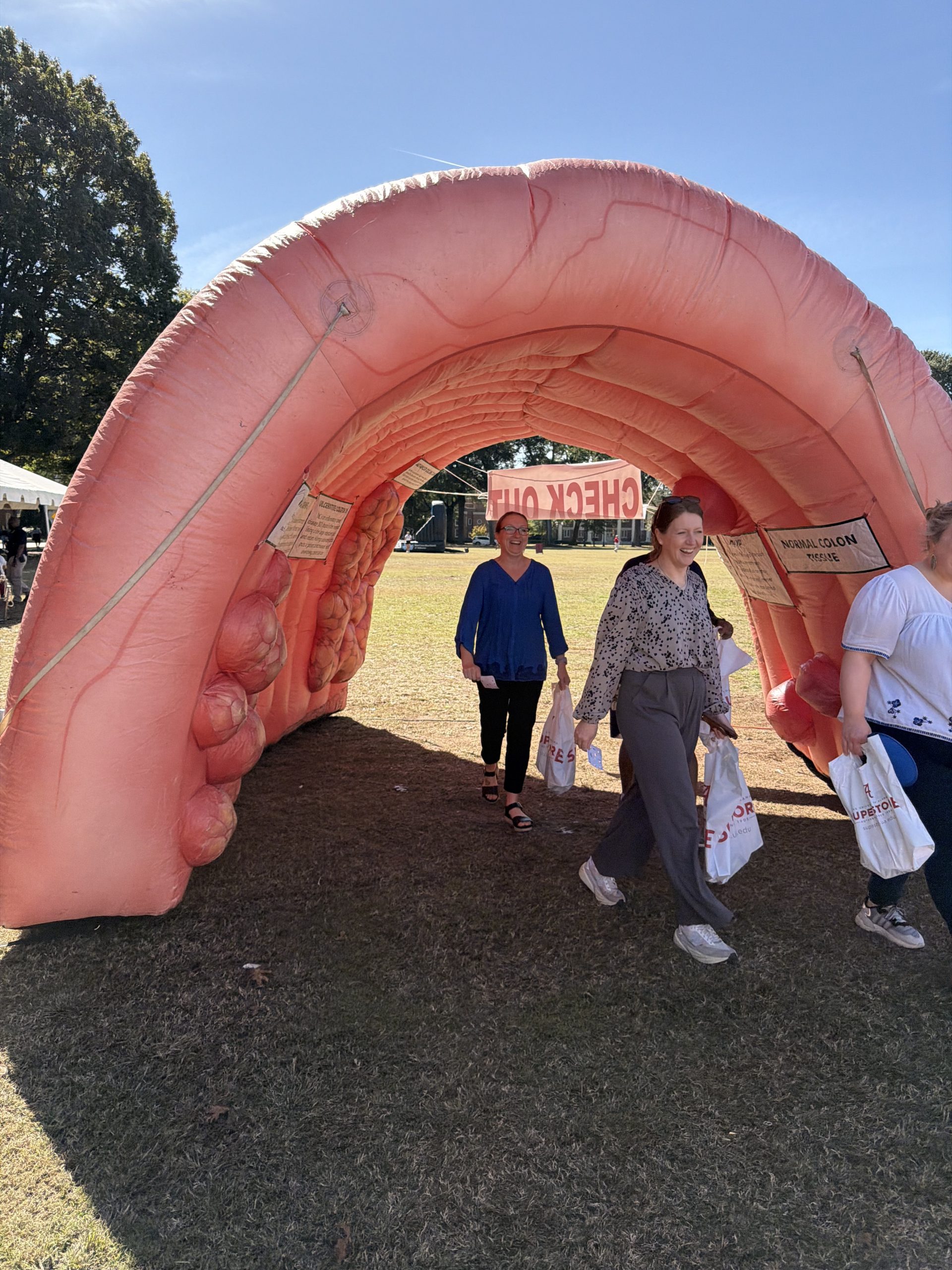 Women smiling as they walk through an inflatable colon outdoors