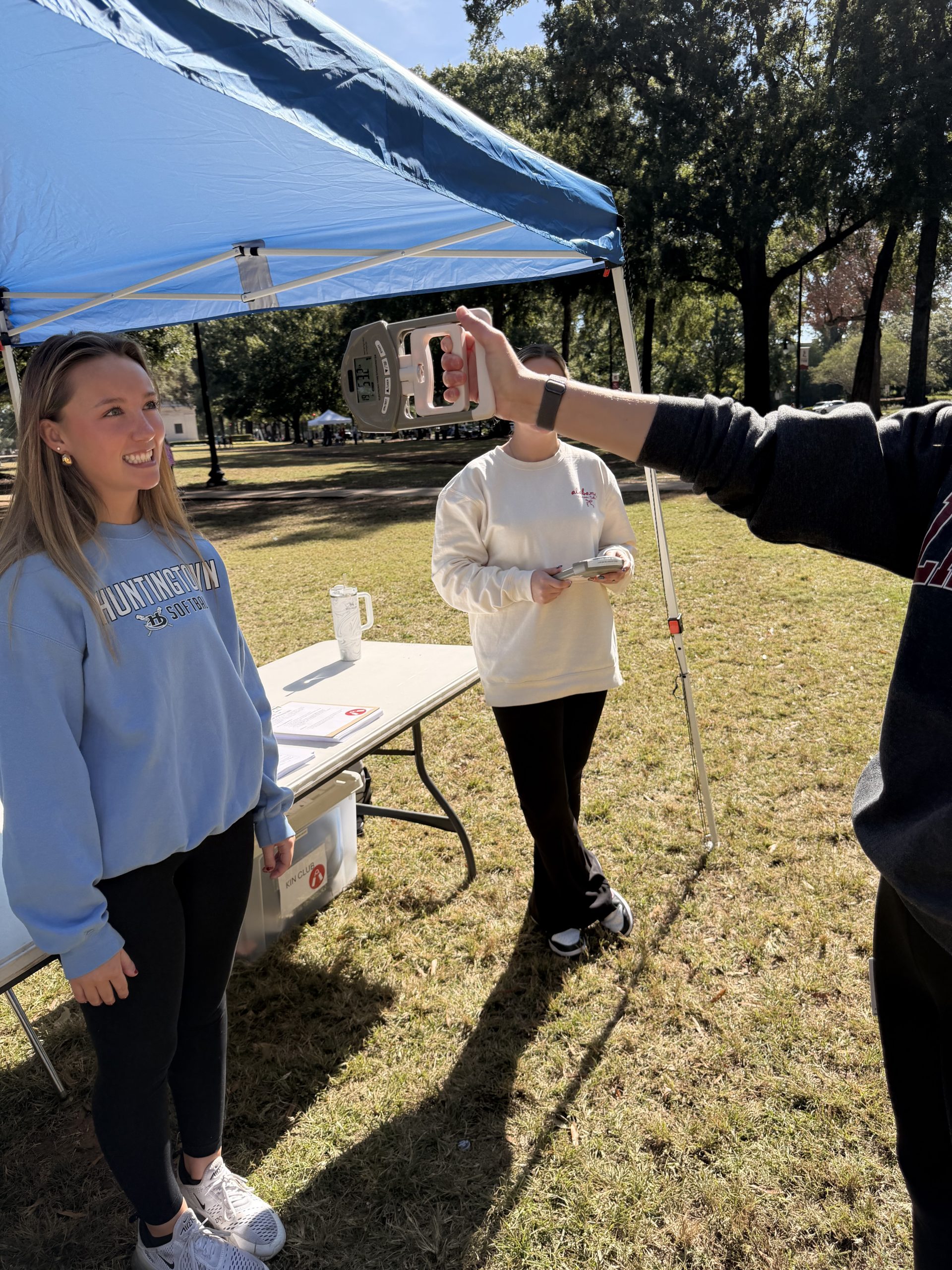 a woman in blue is smiling while looking at someone performing a grip strength test