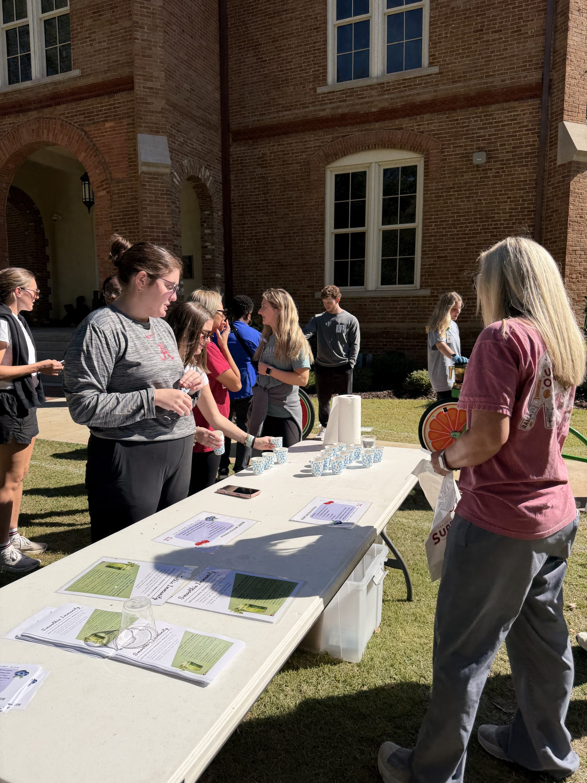students stand by a table talking about the importance of nutrition to quad in motion participants with the use of handouts
