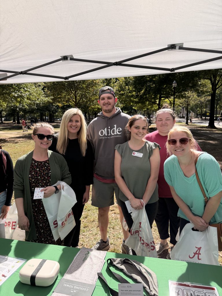 a group of women and one man stand under a tent outdoors smiling at the camera