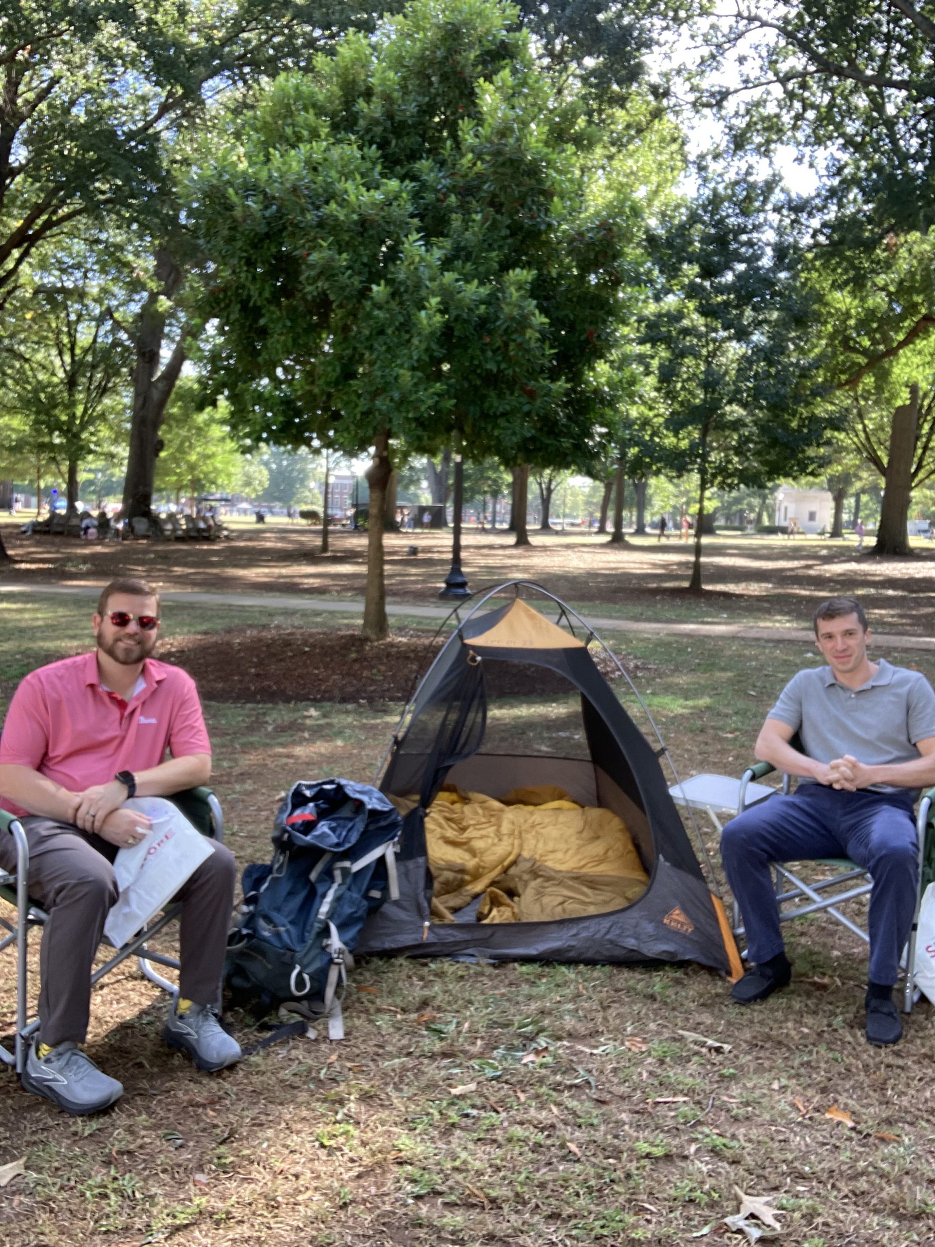 two men sitting in camping chairs with a small camping tent between them