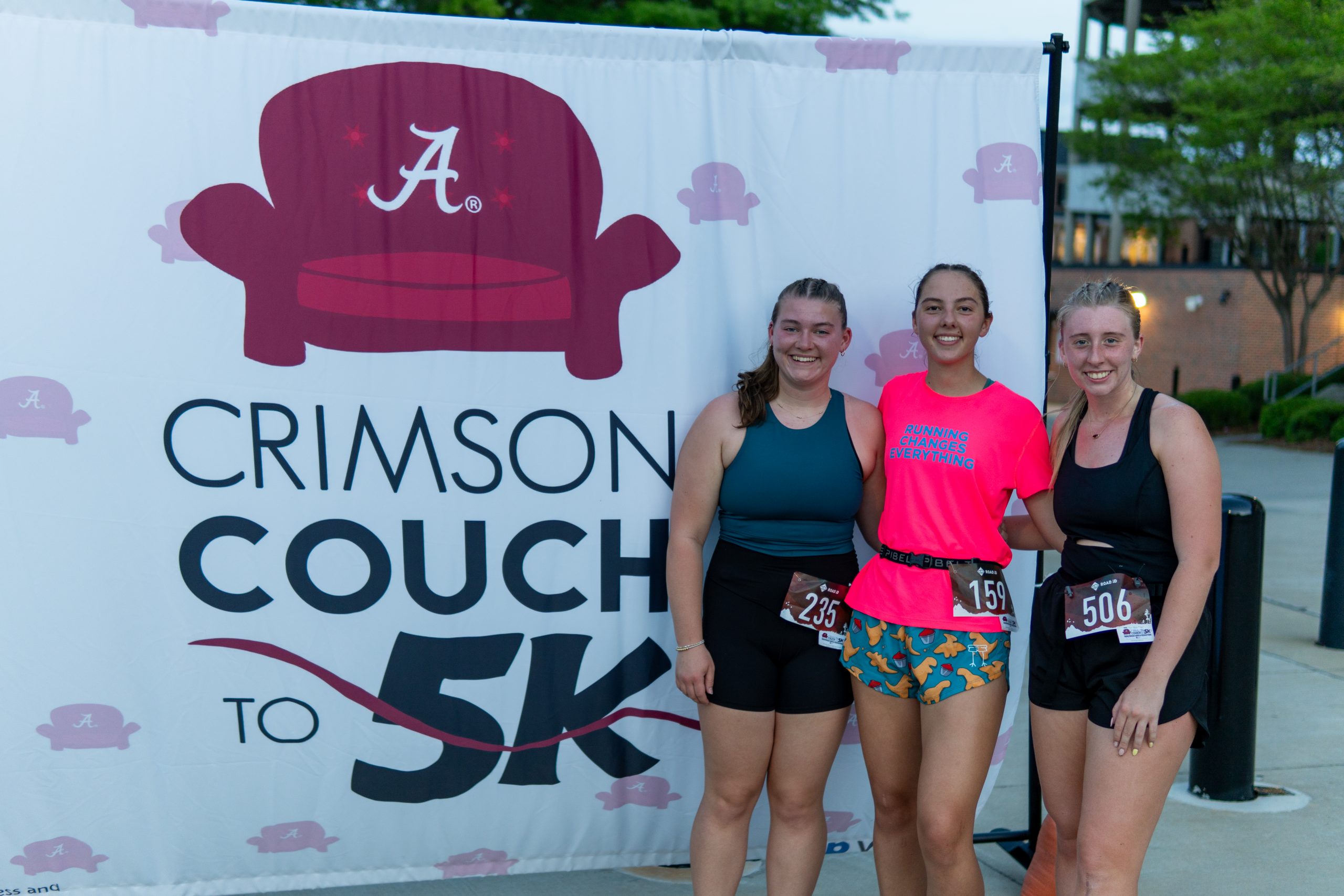 Three women runners standing in front of a CC25K sign