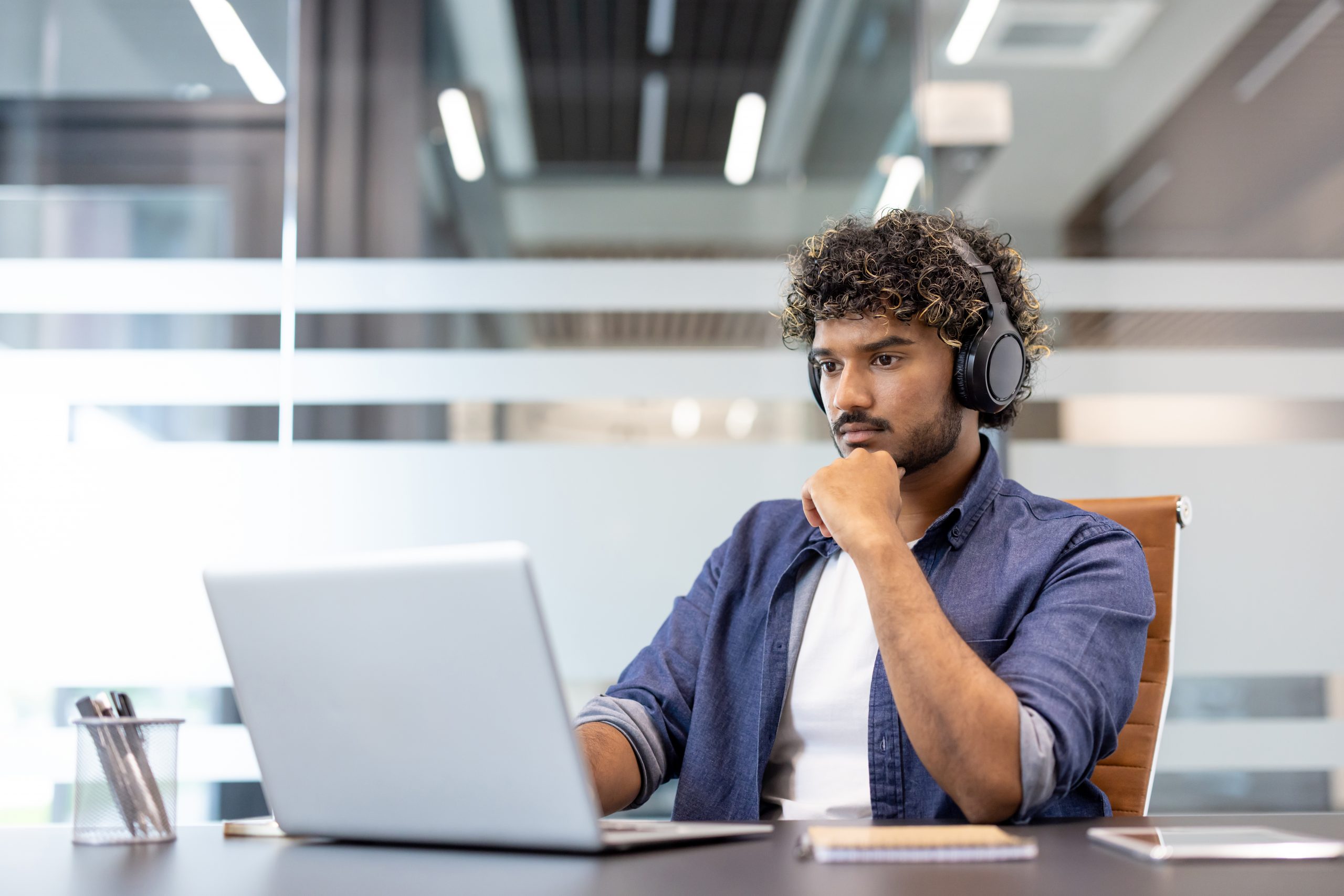 Serious and focused young Indian man in headphones working in the office on a laptop.