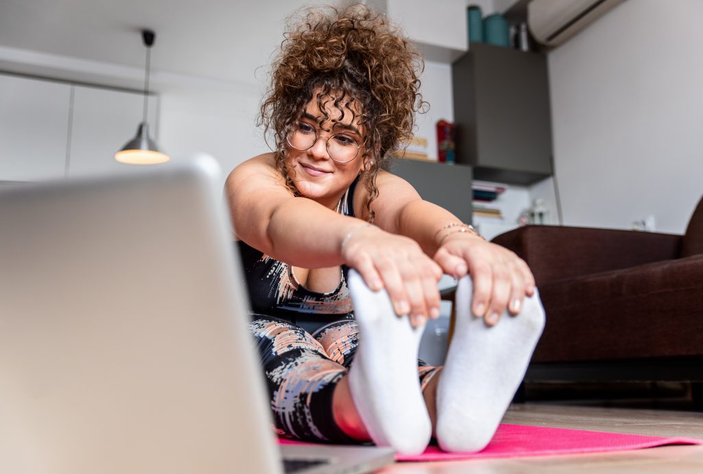 Young woman at home doing exercise in front of open laptop, repeating instructions by professional online fitness trainer.